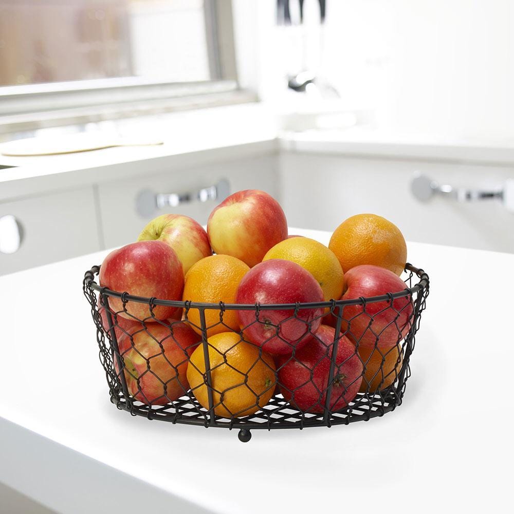 Elegant black wire fruit basket displayed on a dining table filled with colorful fruits.