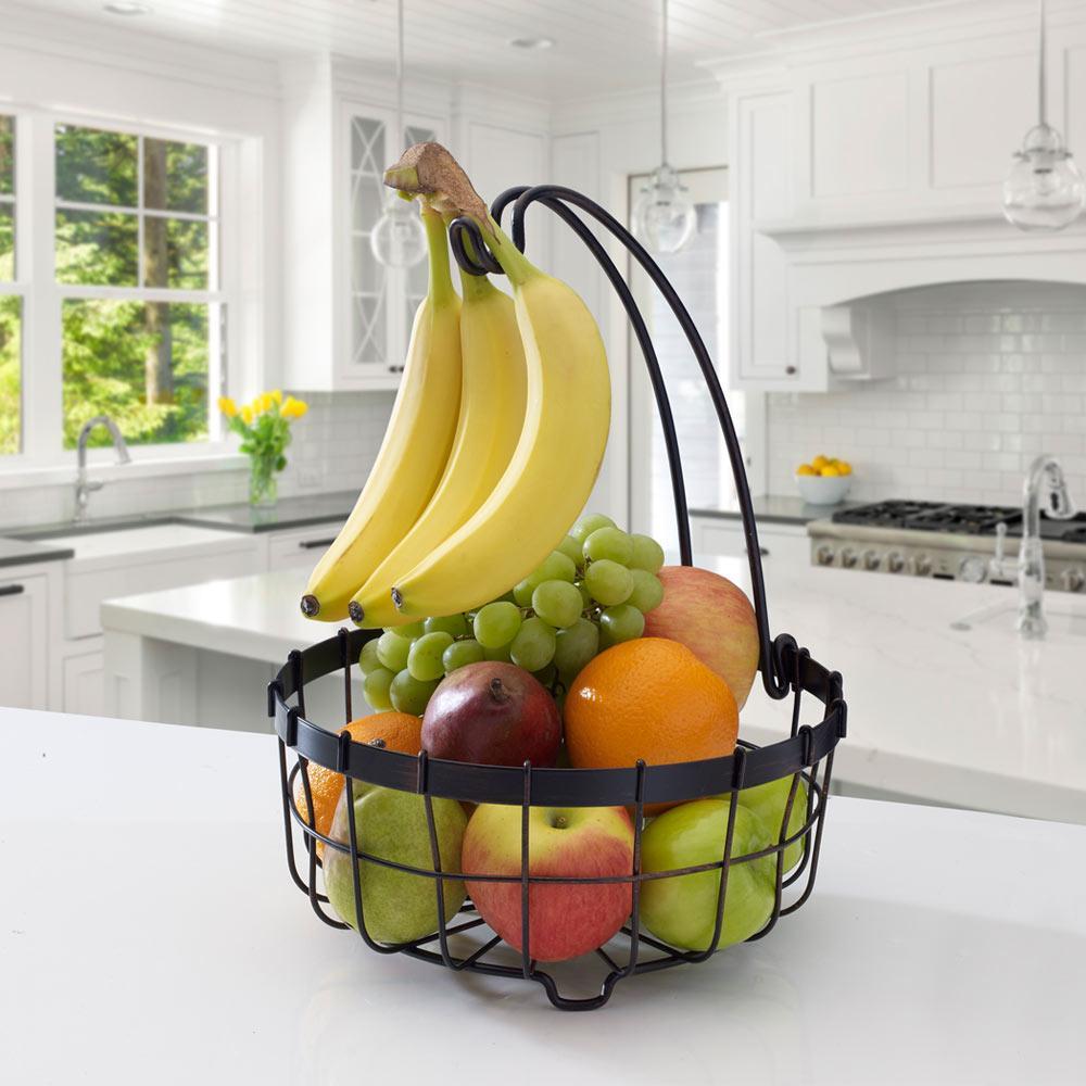 Wrought iron fruit basket with banana hanger displaying bananas and apples.