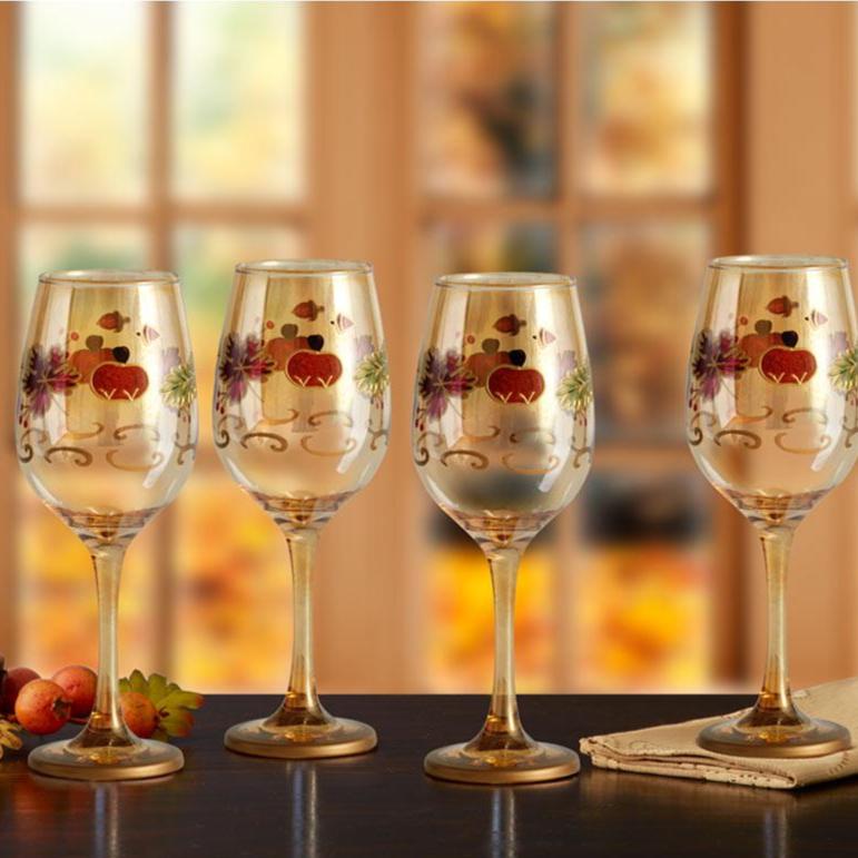 Set of four decorative wine glasses with fall-themed leaf pattern on a wooden table